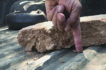 A finger pressing on a block of gravel bound into one solid piece.